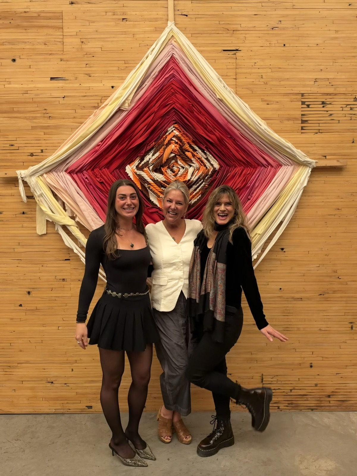 Rachel, Leah and Pneuma smiling together in front of a large woven diamond in pinks and reds