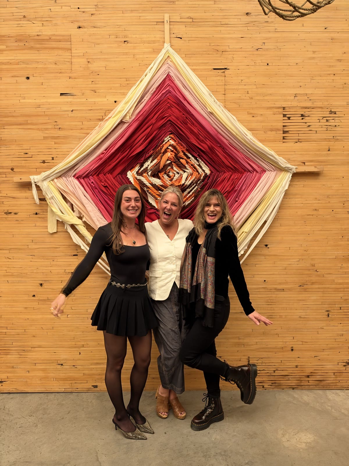 Rachel, Leah and Pneuma laughing together in front of a large woven diamond in pinks and reds